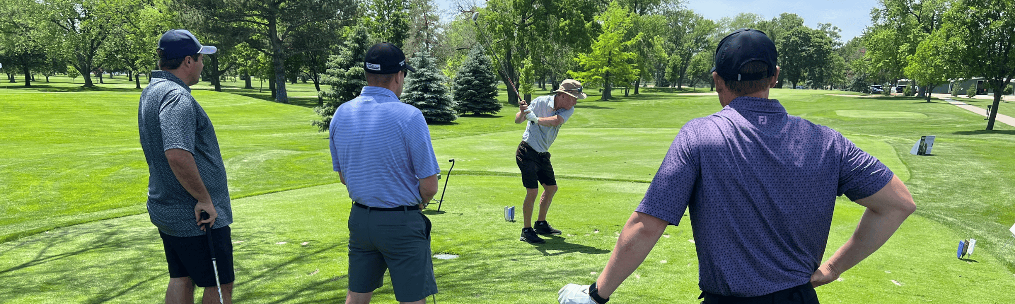 Golfer swings as team watches during 2025 Heartland United Way Golf Tournament