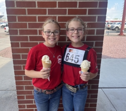 Two girls enjoy ice cream from the Scoops Ice Cream Parlor at the 2024 Nebraska State Fair