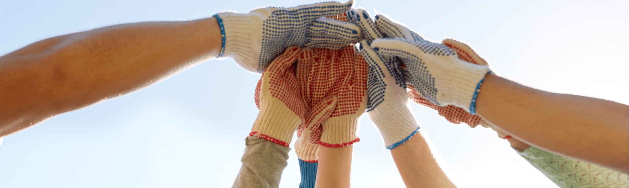 Hands wearing work clothes join together under a blue sky