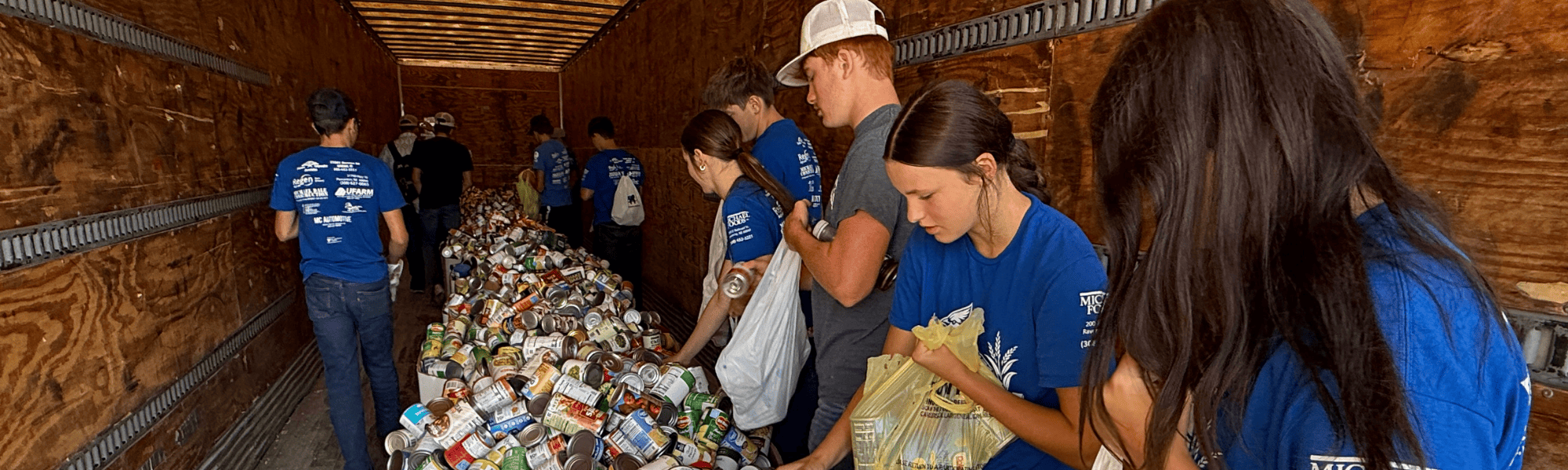FFA students in blue shirts from Ravenna stack canned food inside a trailer at Husker Harvest Days in 2025.