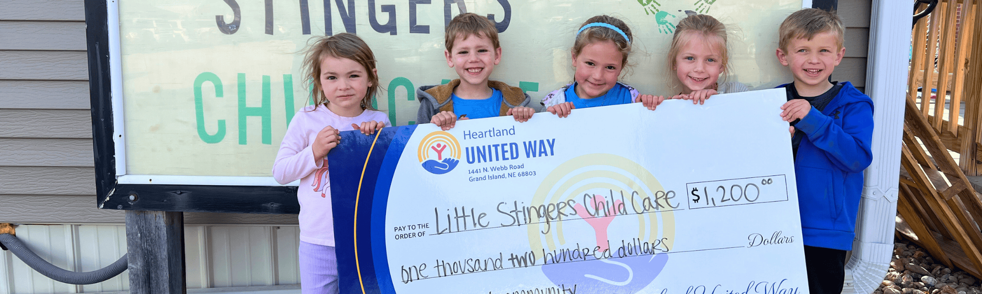 Kids from Little Stingers Child Care hold a Rural Community Impact Grant check in 2025.