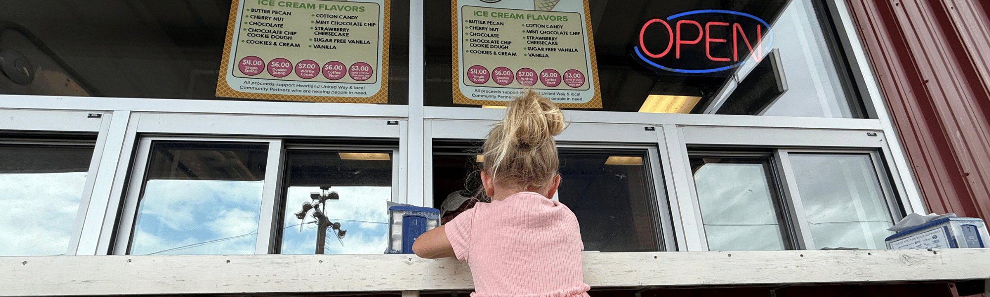 A little girl in pink waits at the SCOOPS Ice Cream Parlor window in 2026.