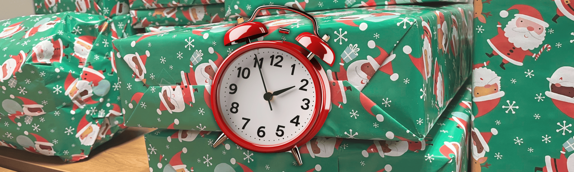 Packages wrapped with green Santa wrapping paper piled on a table with an alarm clock.