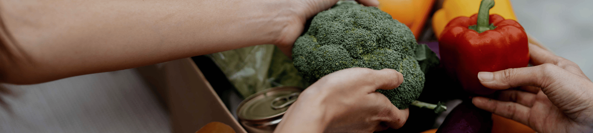 Broccoli and other healthy foods being held as they're taken out of a cardboard box