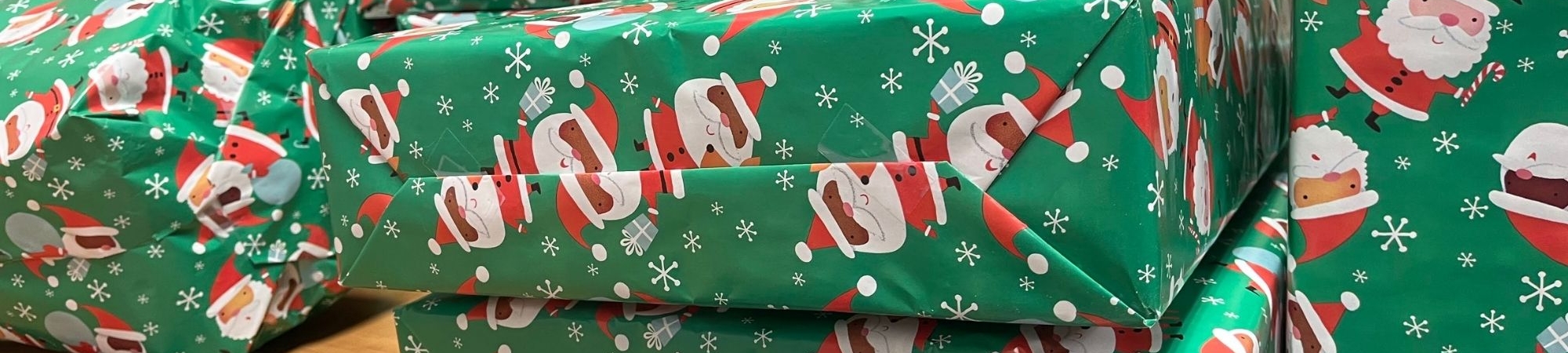 Gifts wrapped in green Santa wrapping paper are piled on a table.