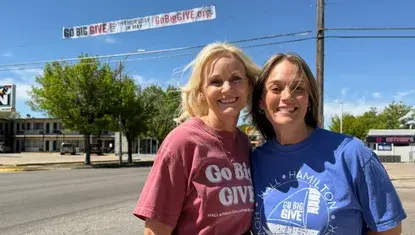 Karen Rathke and Melissa DeLaet stand in front of a Go Big GIVE banner.